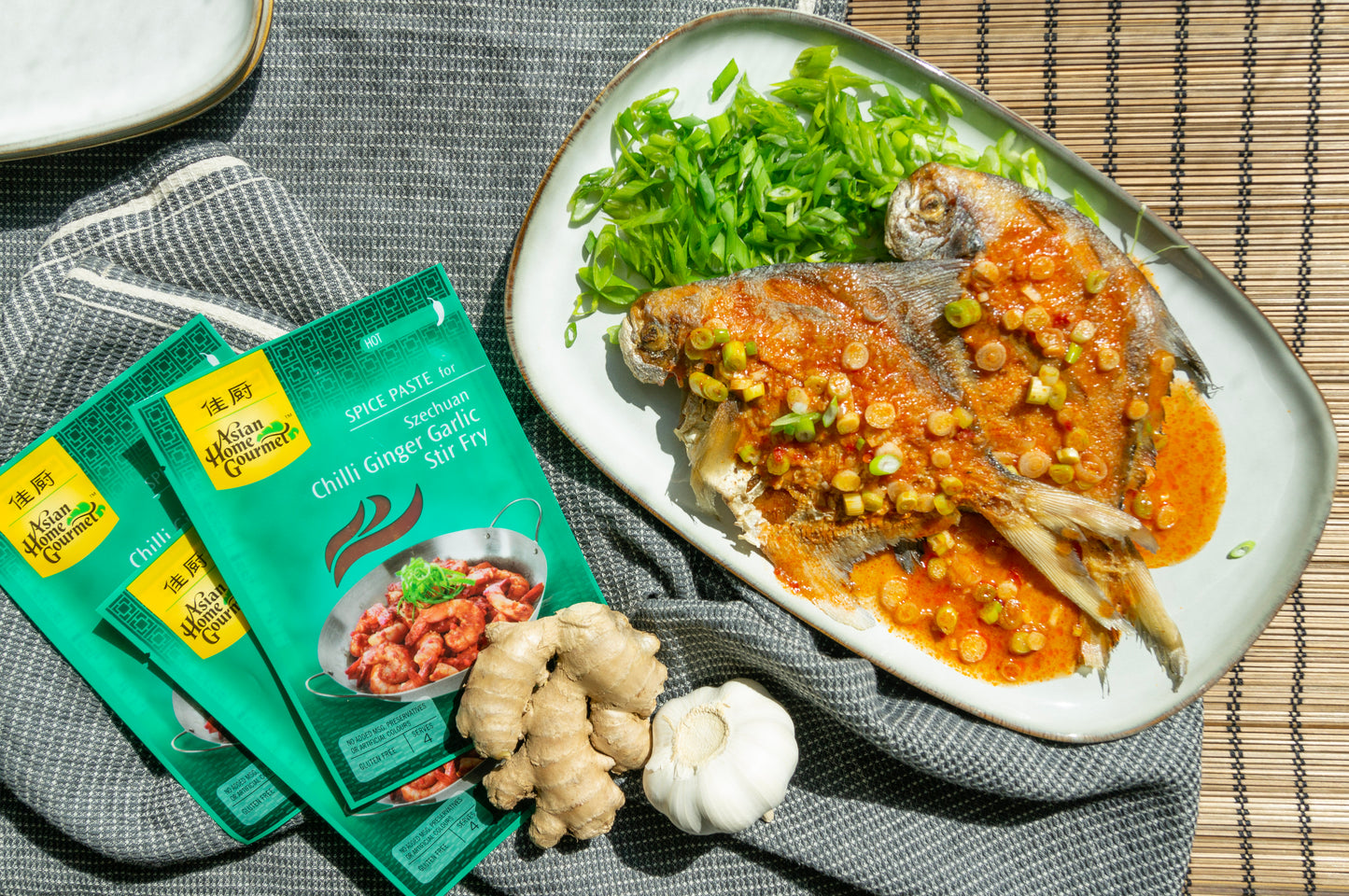 2 pomfret fish in asian home gourmet spice paste for chili ginger garlic stir fry sauce on a white plate.