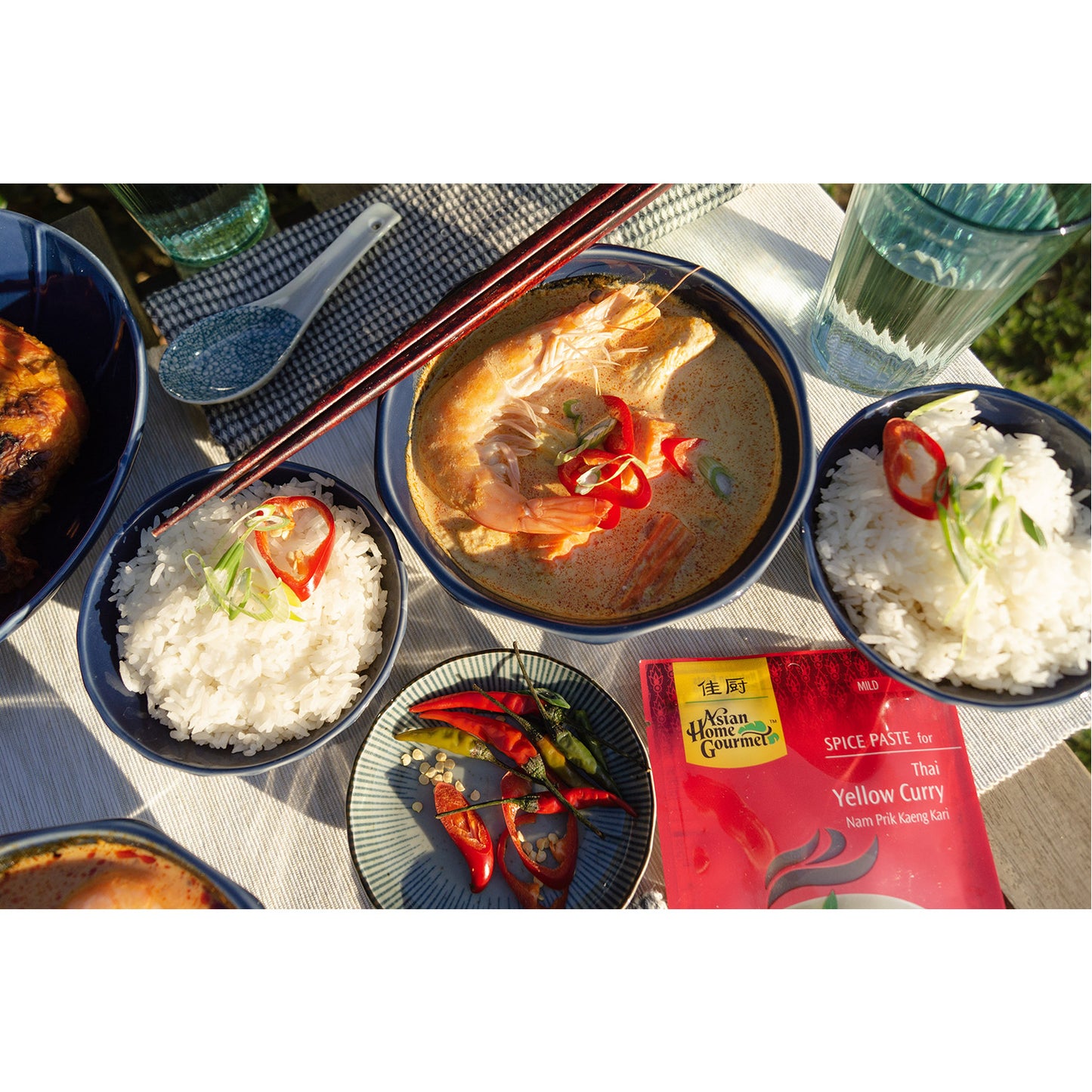 Lifestyle photograph of Thai Seafood Yellow Curry and bowls of rice and fresh chilis in outdoor setting.