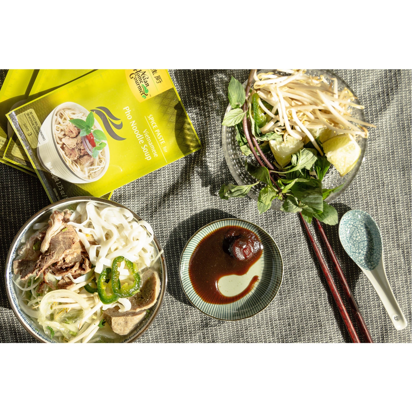 Lifestyle photograph pho bowls with hoisin sauce, bean sprouts, jalapenos, and lime.