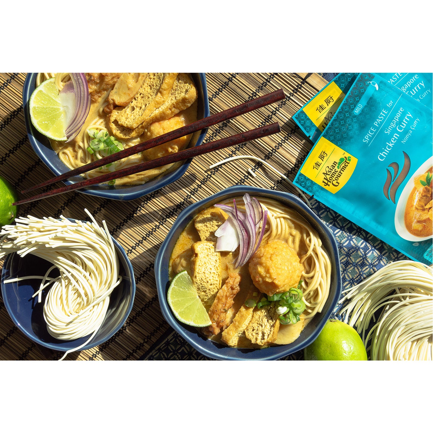 A lifestyle photograph of chicken curry bowls with noodles, tofu, lime, and onion.