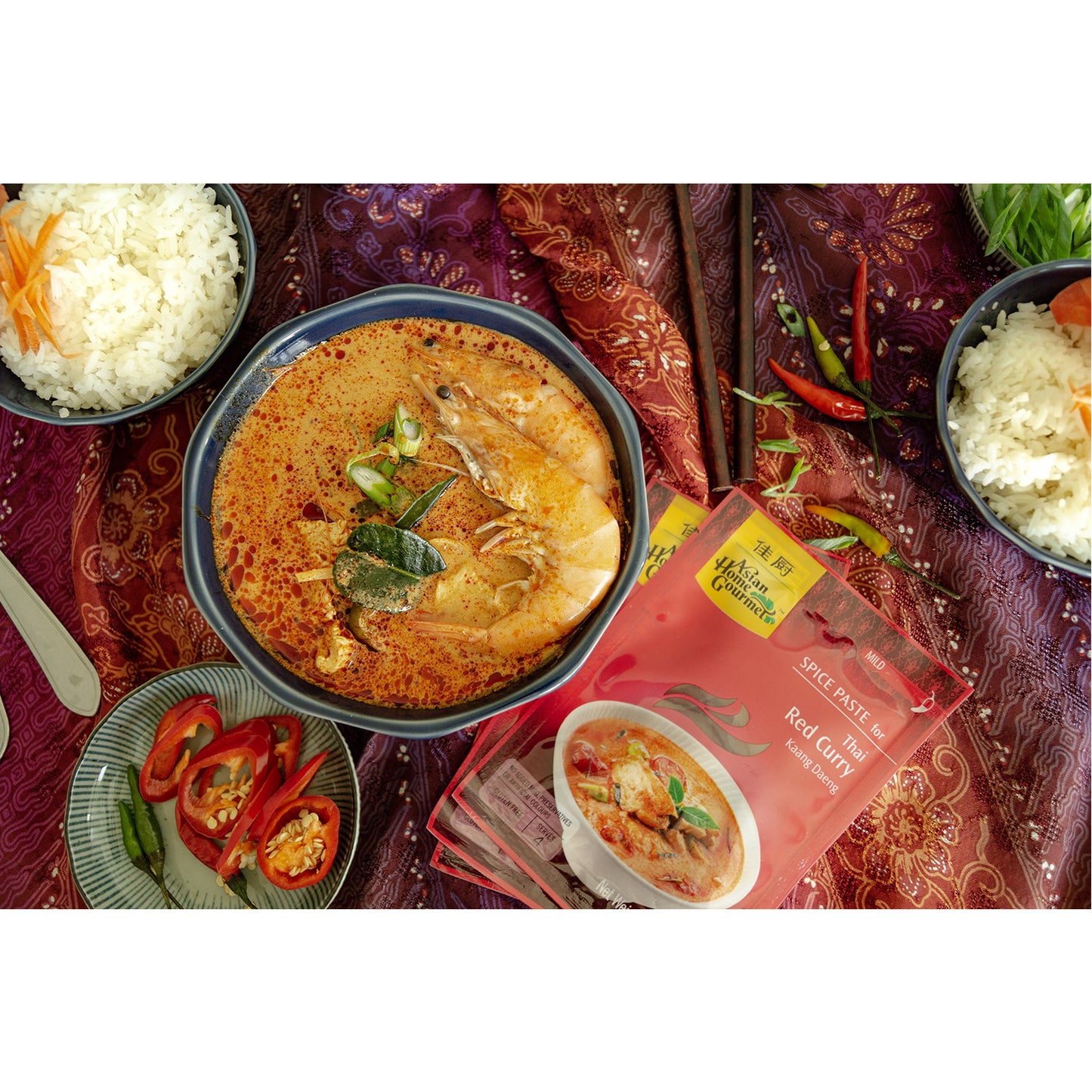 lifestyle photograph of Thai Cuisine, seafood red curry with a side of fresh chilis and two bowls of rice.