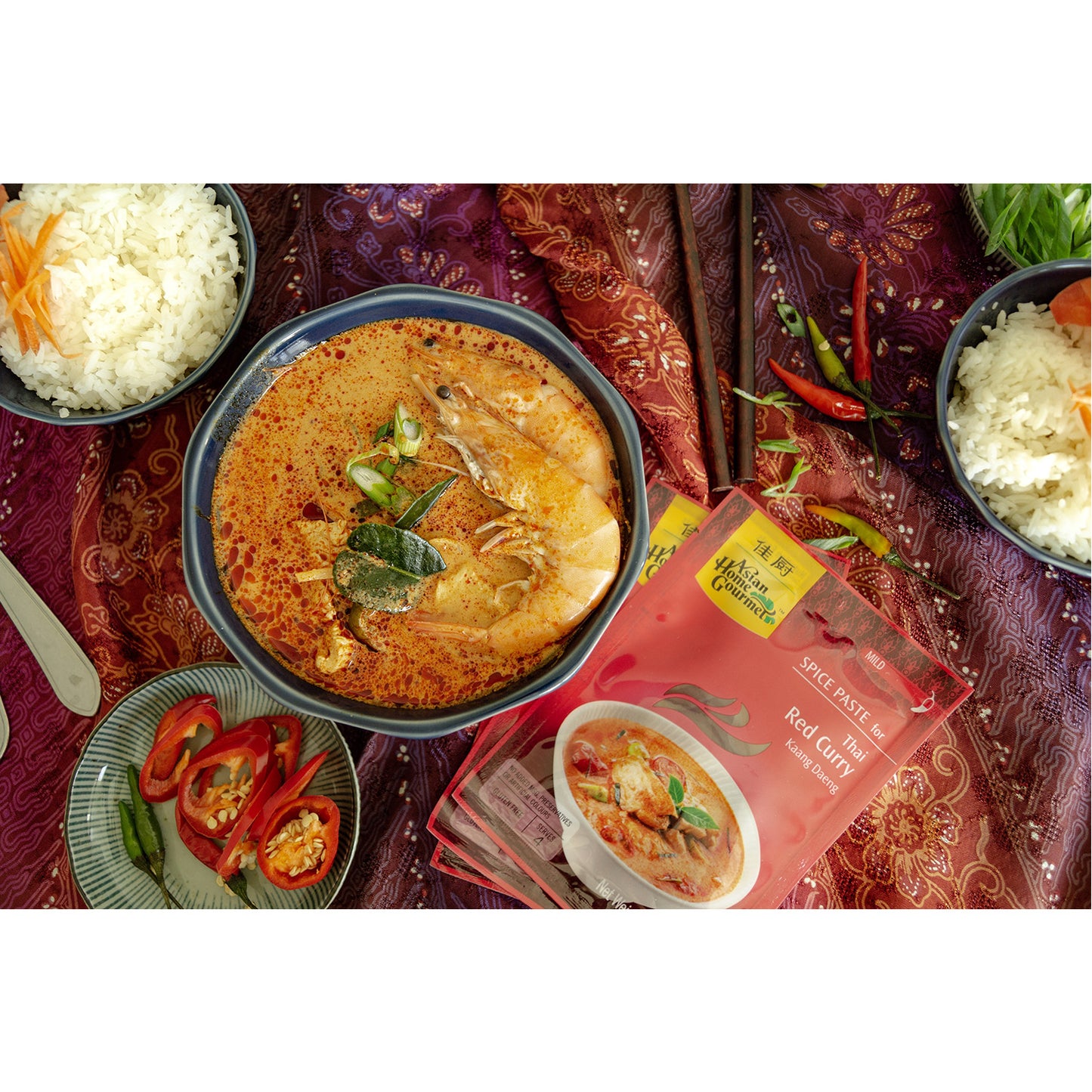lifestyle photograph of Thai Cuisine, seafood red curry with a side of fresh chilis and two bowls of rice. 
